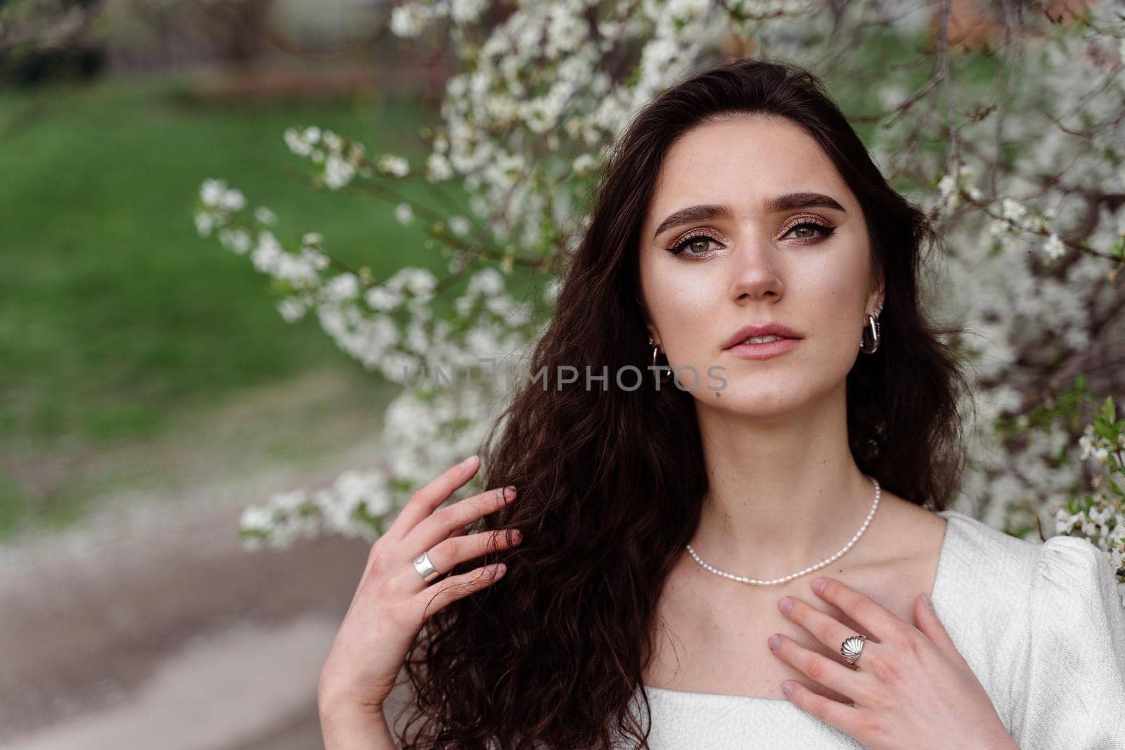 Spring lifestyle. Model posing near white blooming trees without mask outdoor countryside. Dreaming girl with curly hair