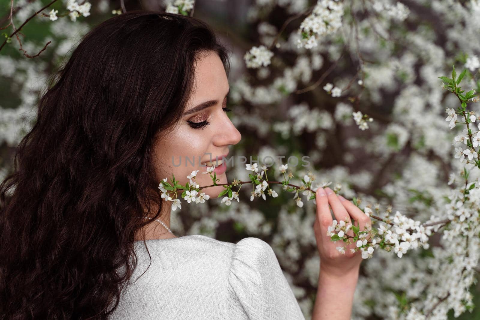 Girl touches and sniffs a branch of a white flowering tree without medical mask. Spring walking in the park