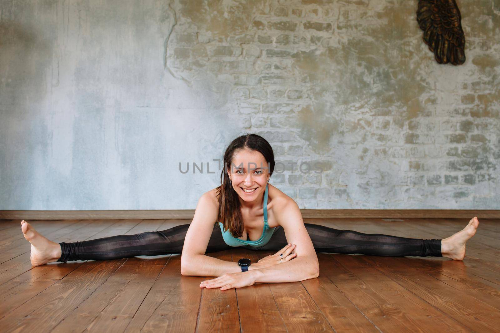 Yoga girl lies on the floor, on a wide splits and smiles