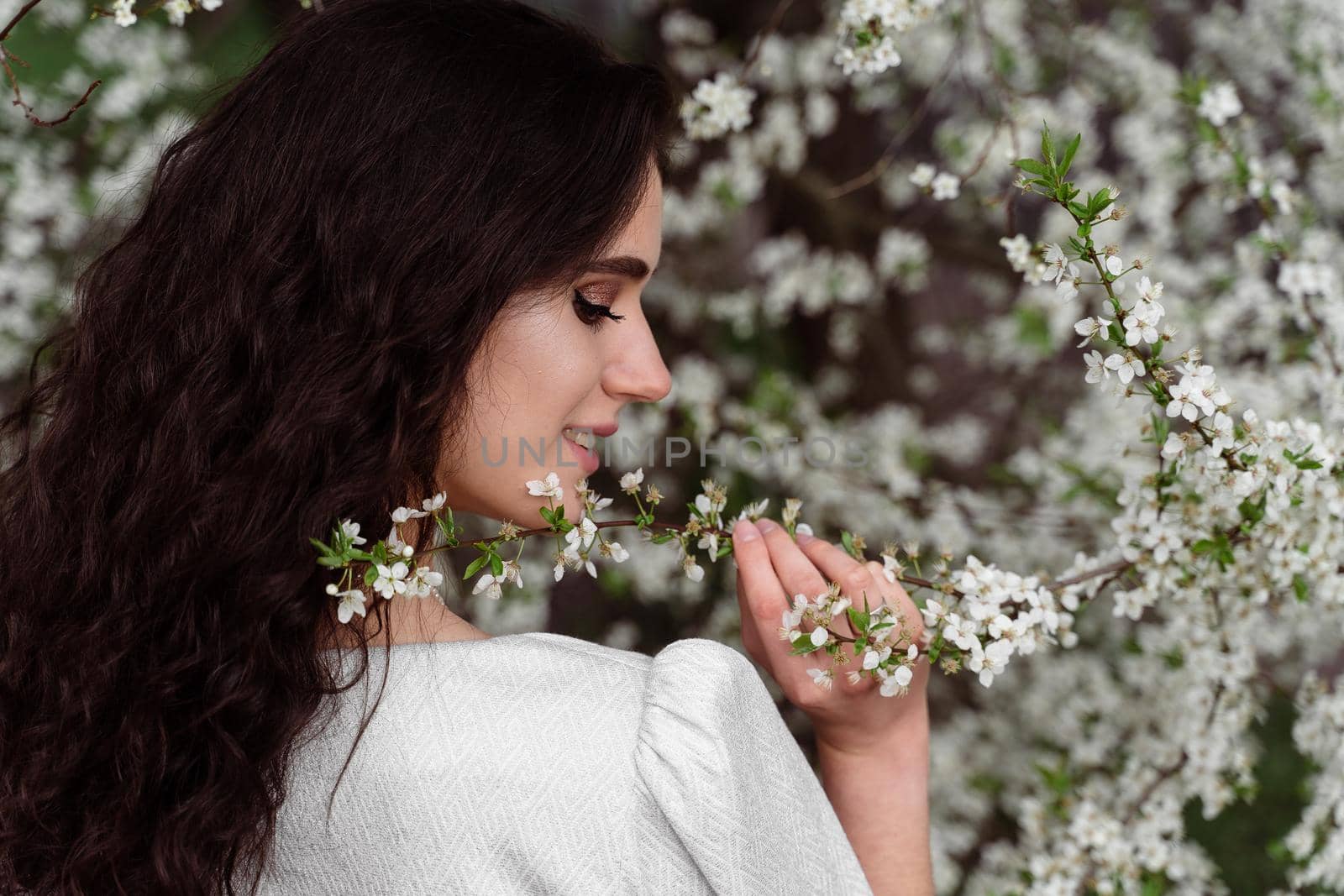 Girl touches and sniffs a branch of a white flowering tree without medical mask. Spring walking in the park