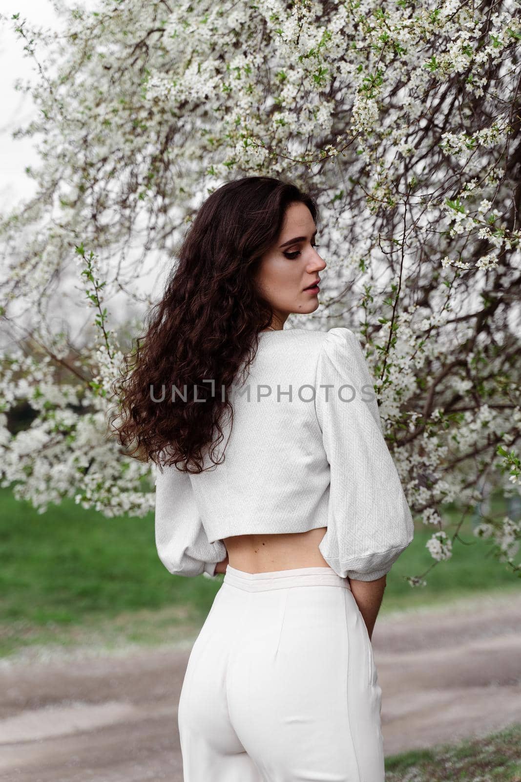 Portrait of young woman in the garden. Attractive girl weared white dress posing near blooming trees