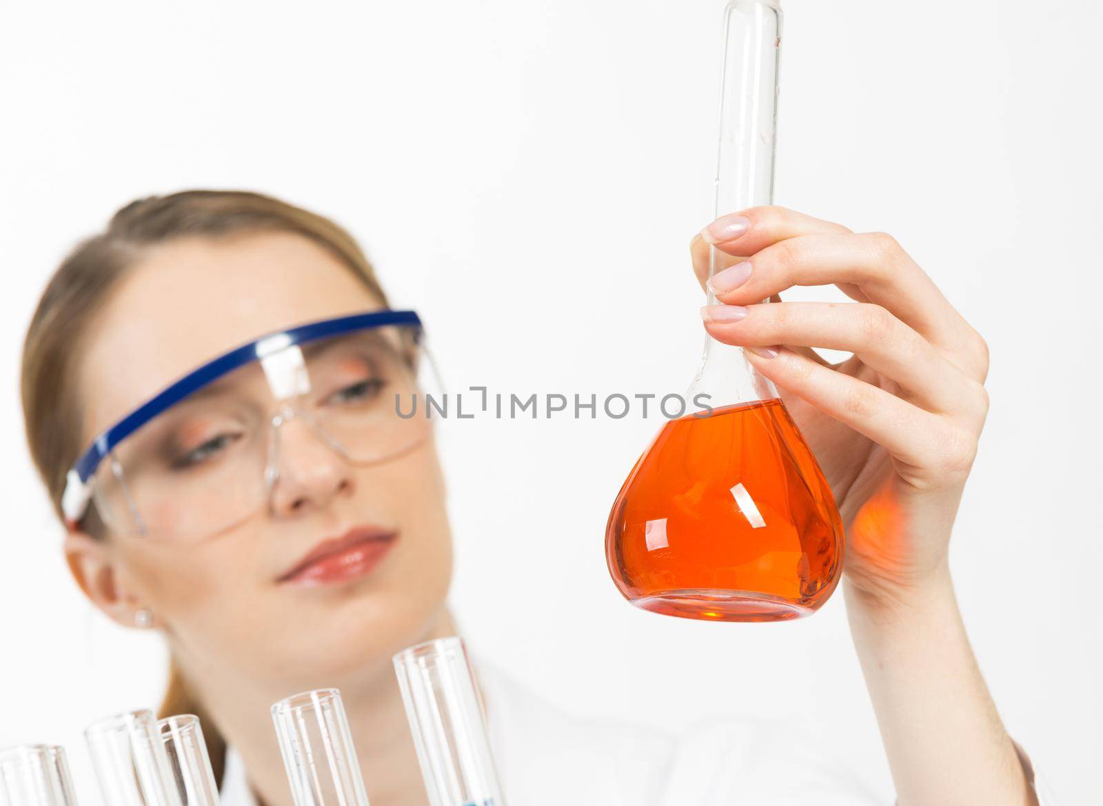 High tech chemical industry concept with female scientist. Young woman laboratory technician in protective goggles looking at flask with liquid in hand. Biochemistry and molecular biology industry.