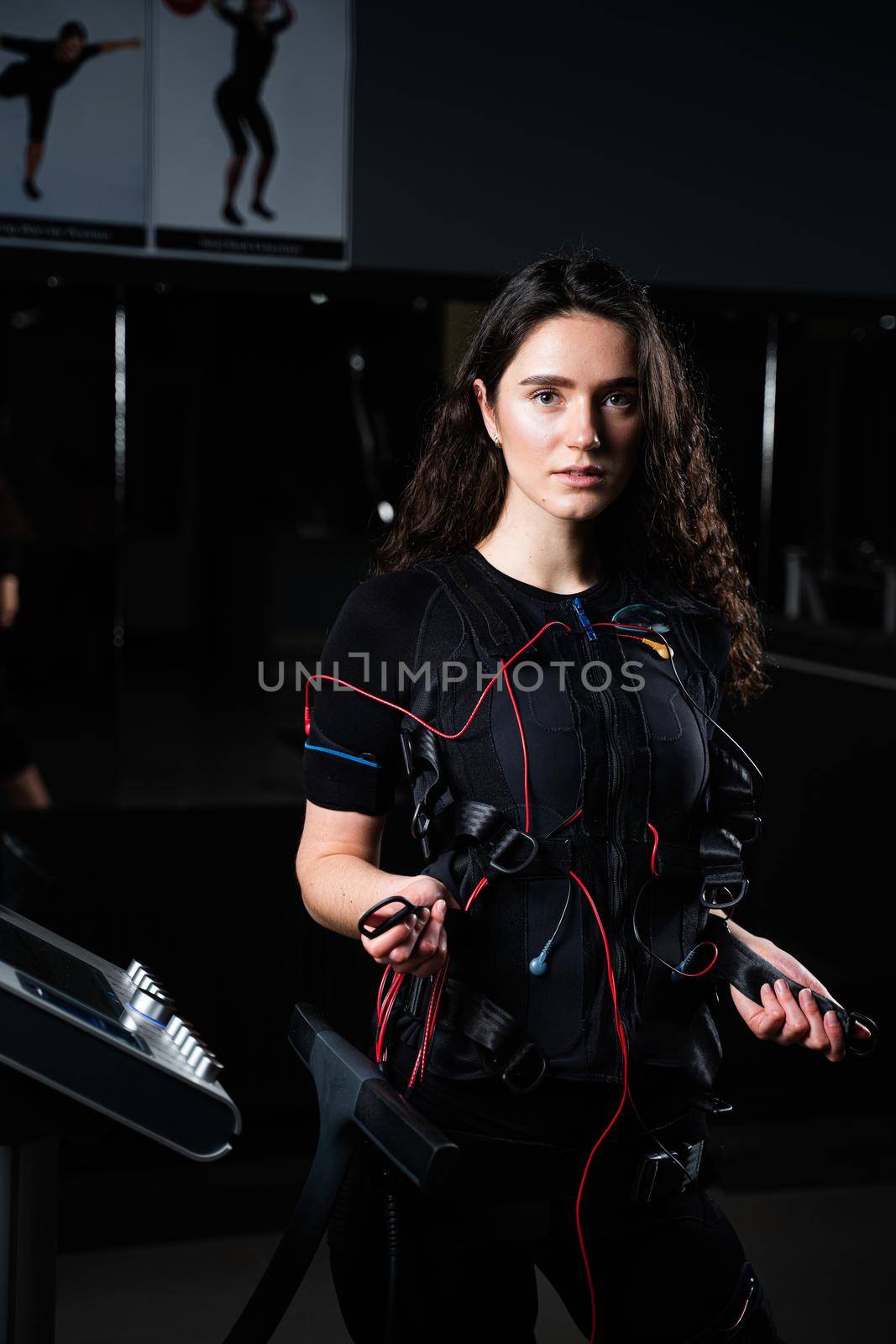 Girl in EMS suit in gym. Sport training in electrical muscle stimulation suit. Making physical exercises.