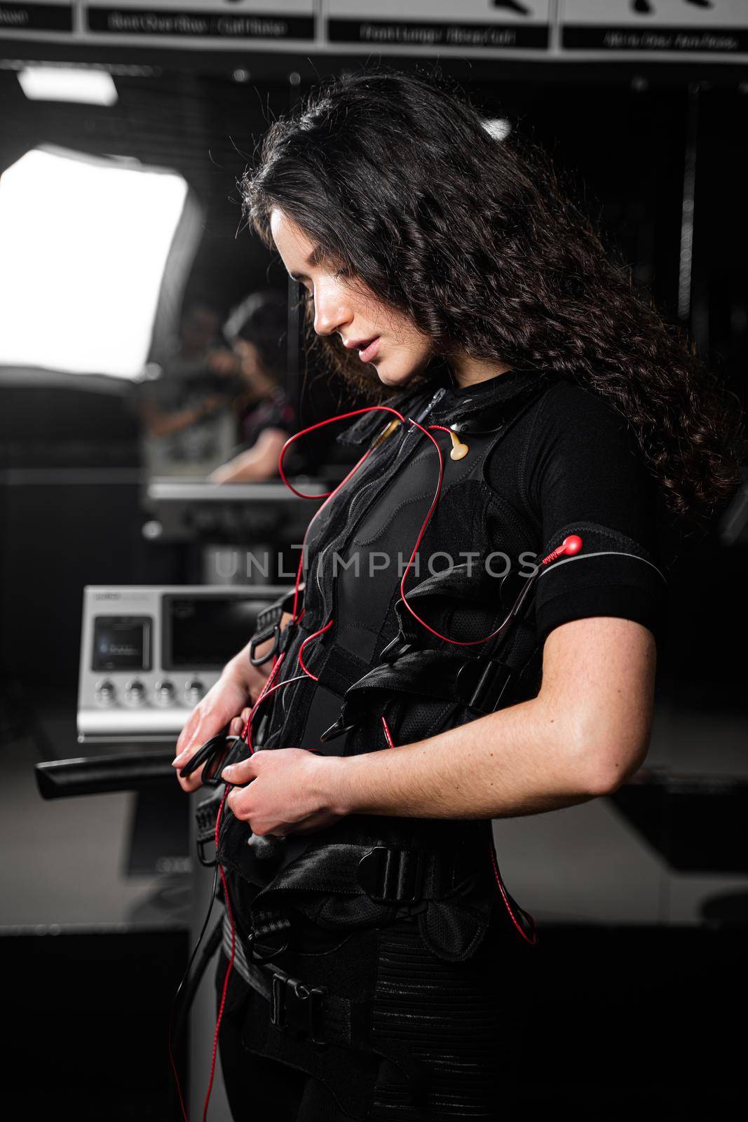 Girl in EMS suit in gym. Sport training in electrical muscle stimulation suit. Making physical exercises by Rabizo