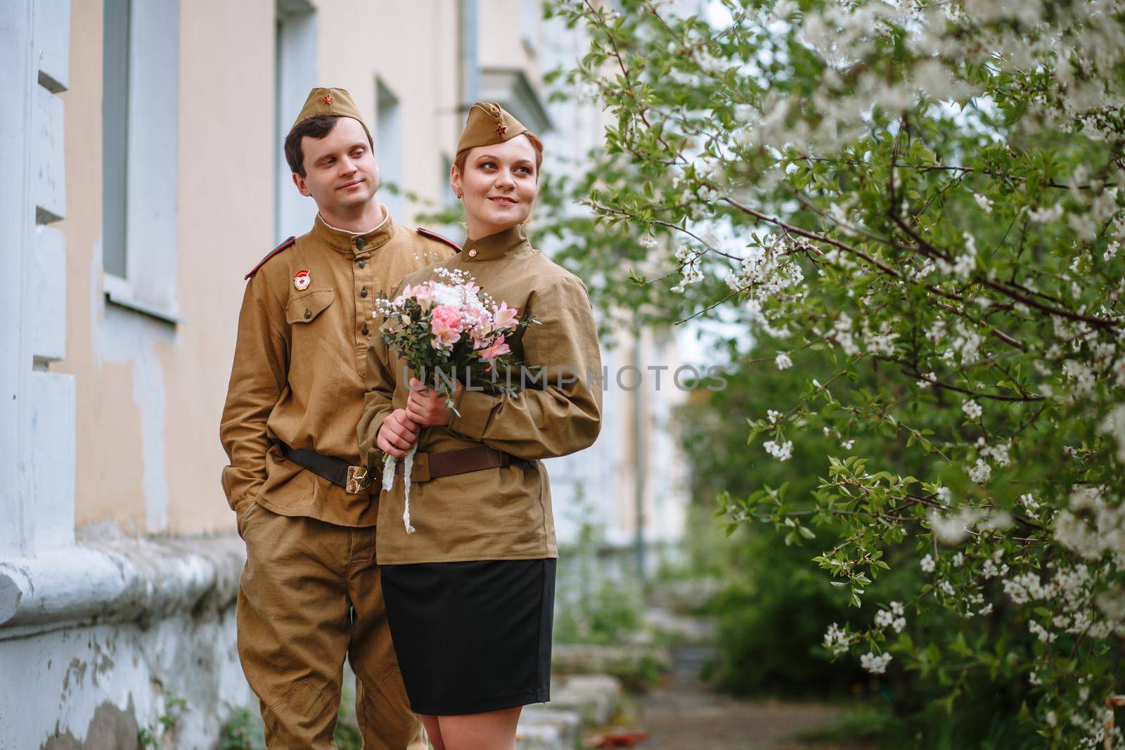 Portrait of two military lovers at a flowering tree. Warm spring, people are returning from the war