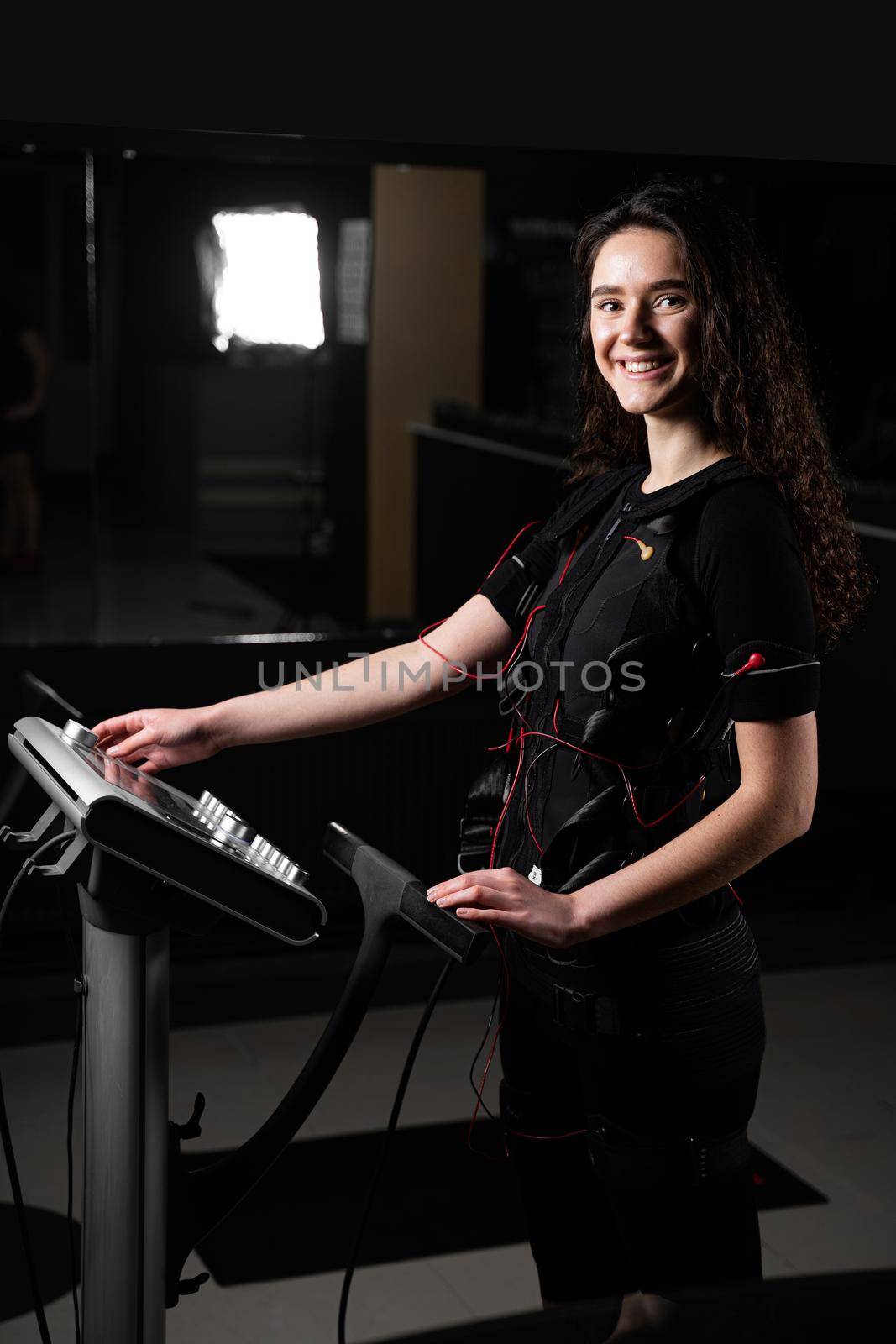 Girl in EMS suit in gym. Sport training in electrical muscle stimulation suit