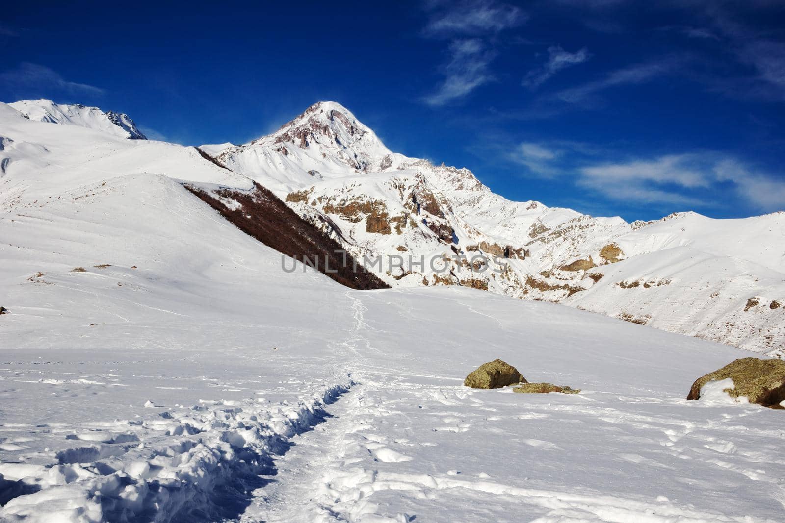 Hiking trail in the mountains. Landscape with snow-capped mountain peaks and clouds in the blue sky. The footpath leads to the foot of the Caucasus Mountains. Caucasian mountains.