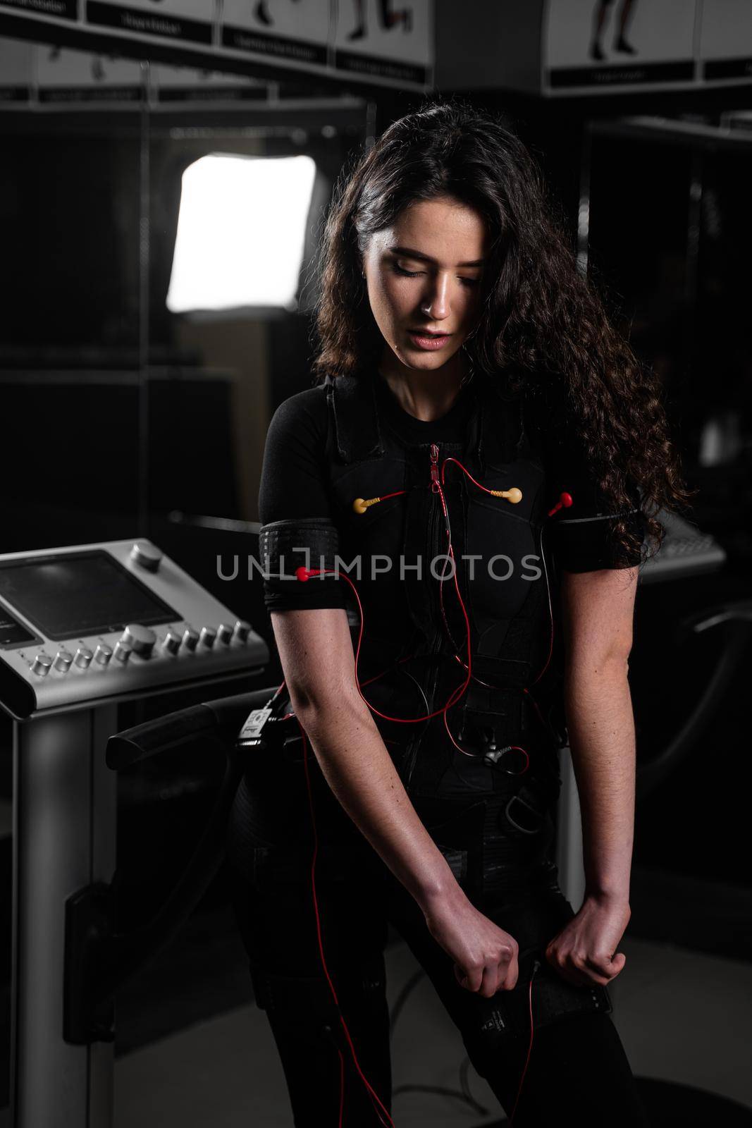 Girl in EMS suit in gym. Sport training in electrical muscle stimulation suit. Making physical exercises.