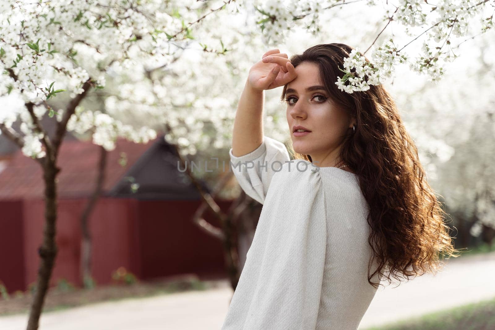 Lovely girl near blooming trees in the park. Outdoor walking in at sunny day. Lifestyle of young woman.