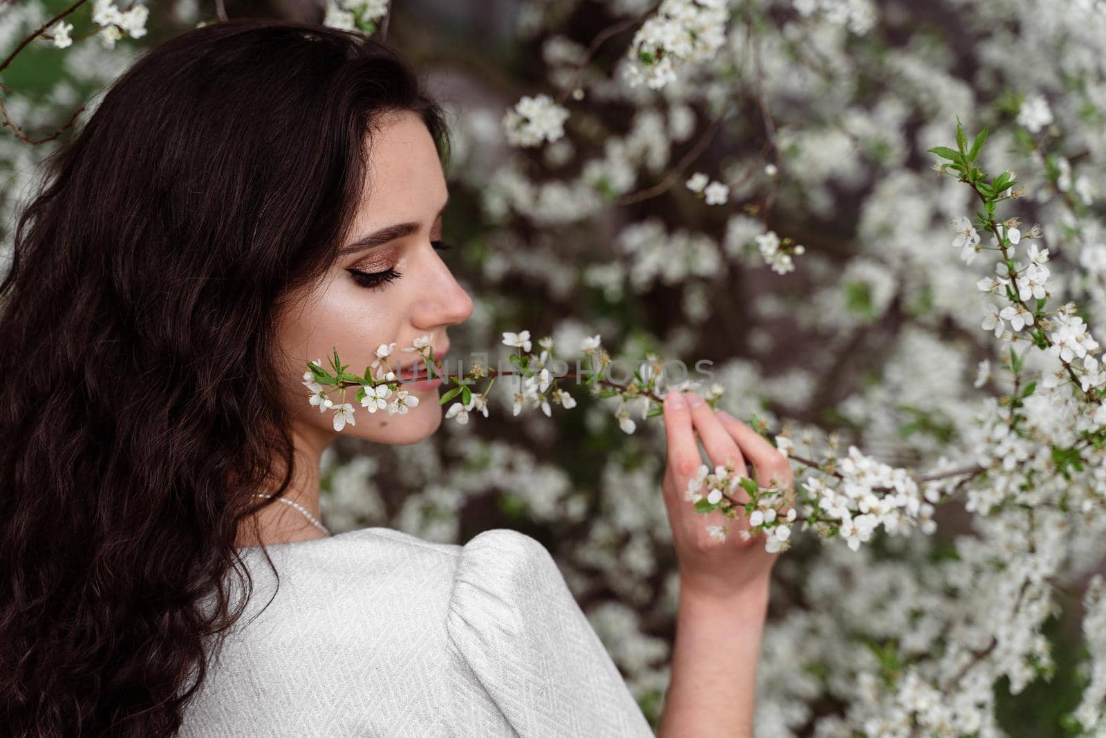 Girl touches and sniffs a branch of a white flowering tree without medical mask. Spring walking in the park