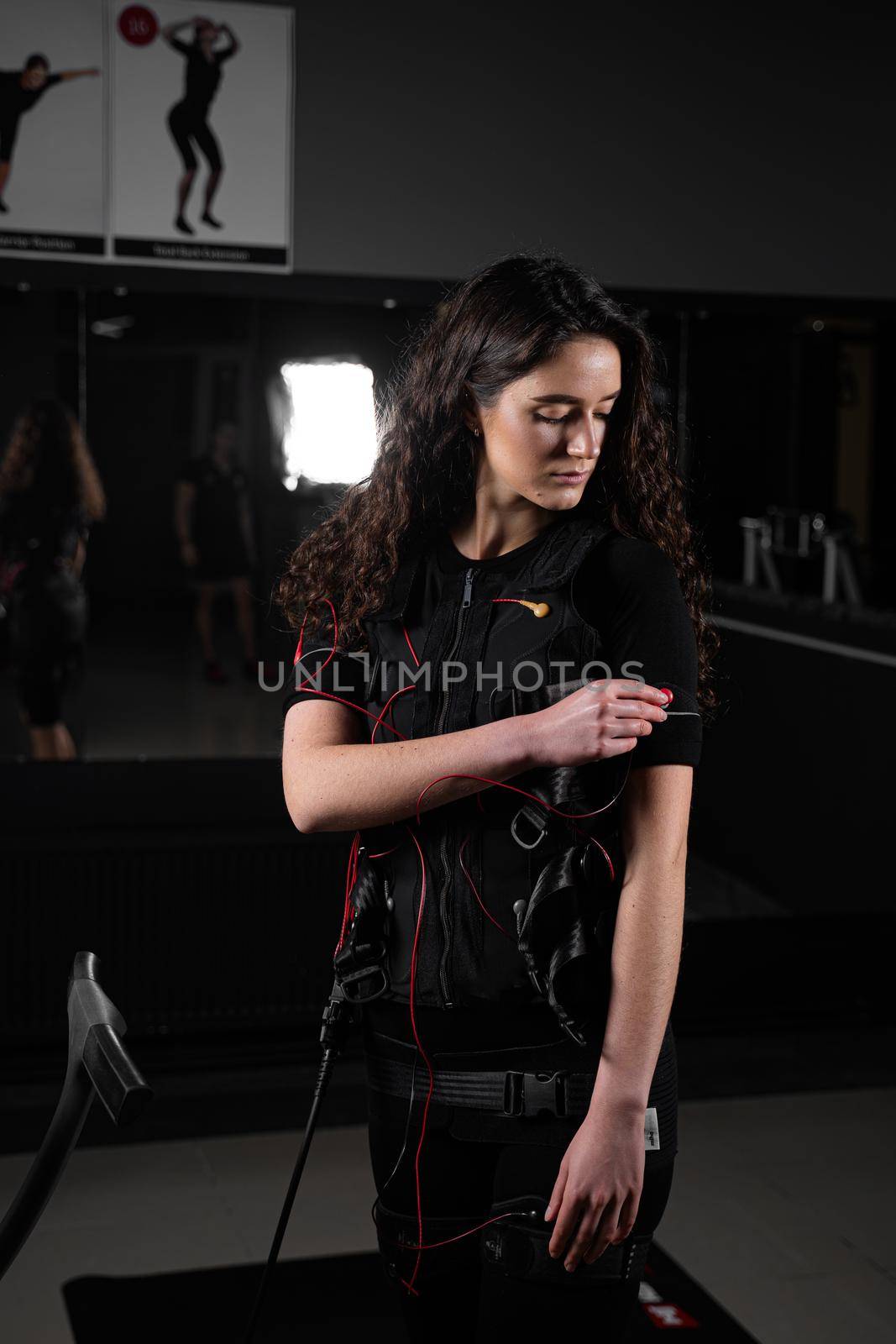 Girl in EMS suit in gym. Sport training in electrical muscle stimulation suit