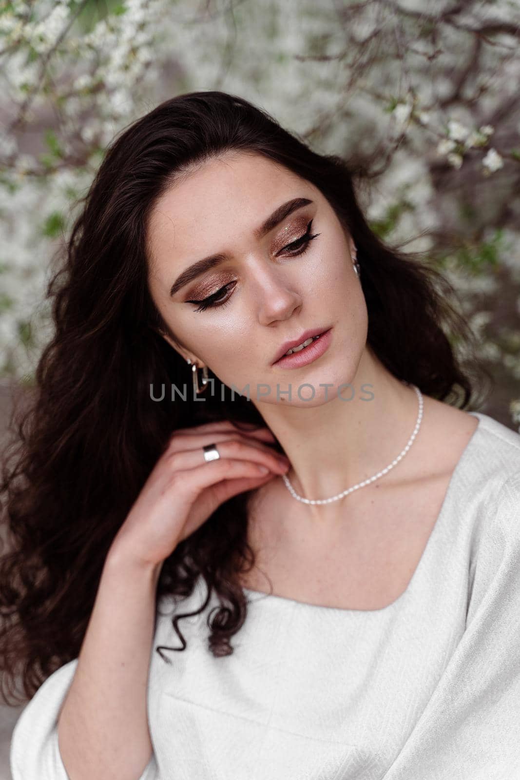 Spring lifestyle. Model posing near white blooming trees without mask outdoor countryside. Dreaming girl with curly hair