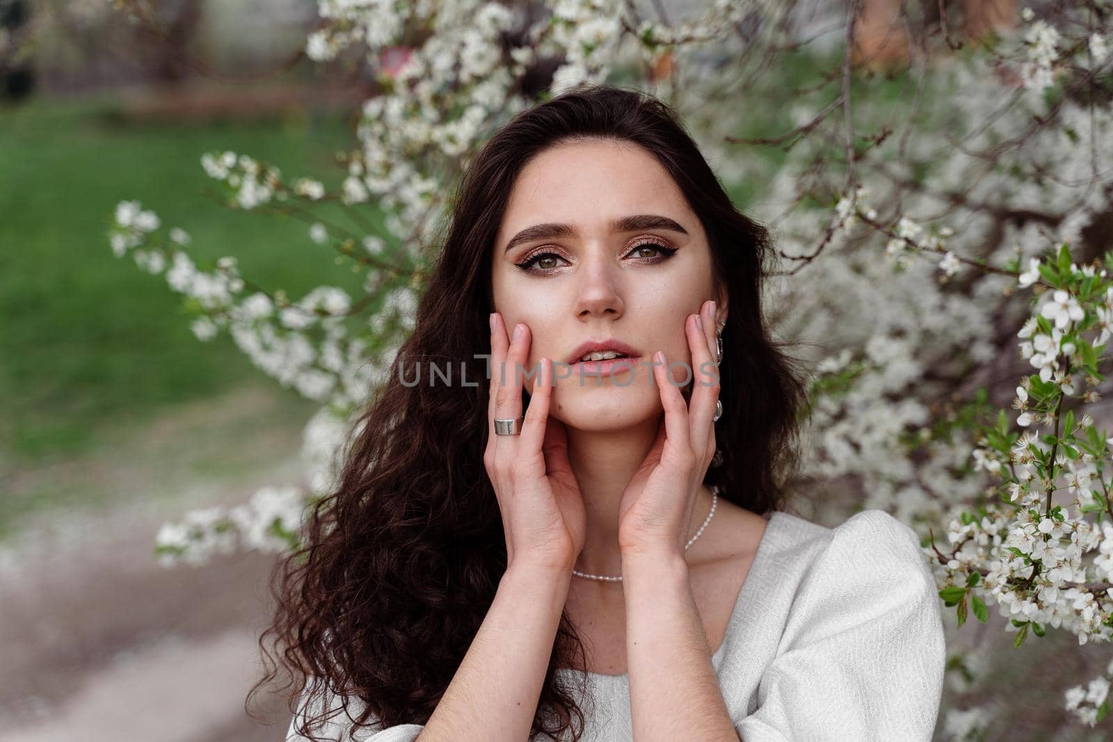 Spring lifestyle. Model posing near white blooming trees without mask outdoor countryside. Dreaming girl with curly hair