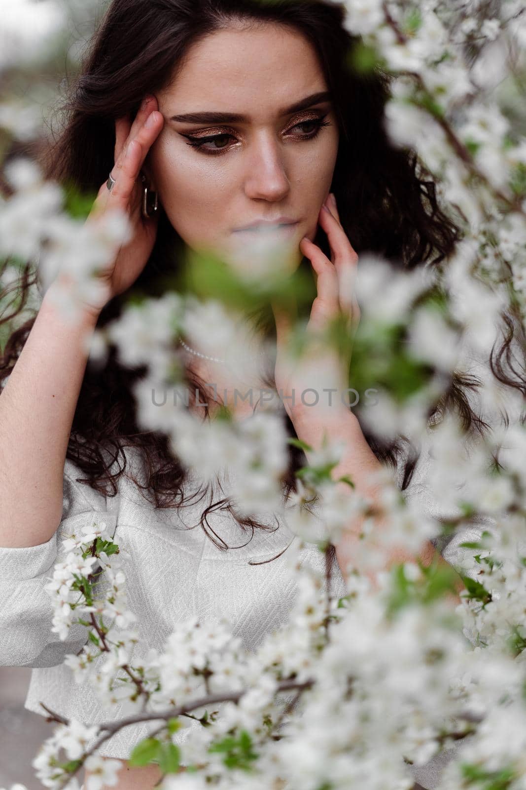 Portrait of young woman in the garden. Attractive girl weared white dress posing near blooming trees. by Rabizo
