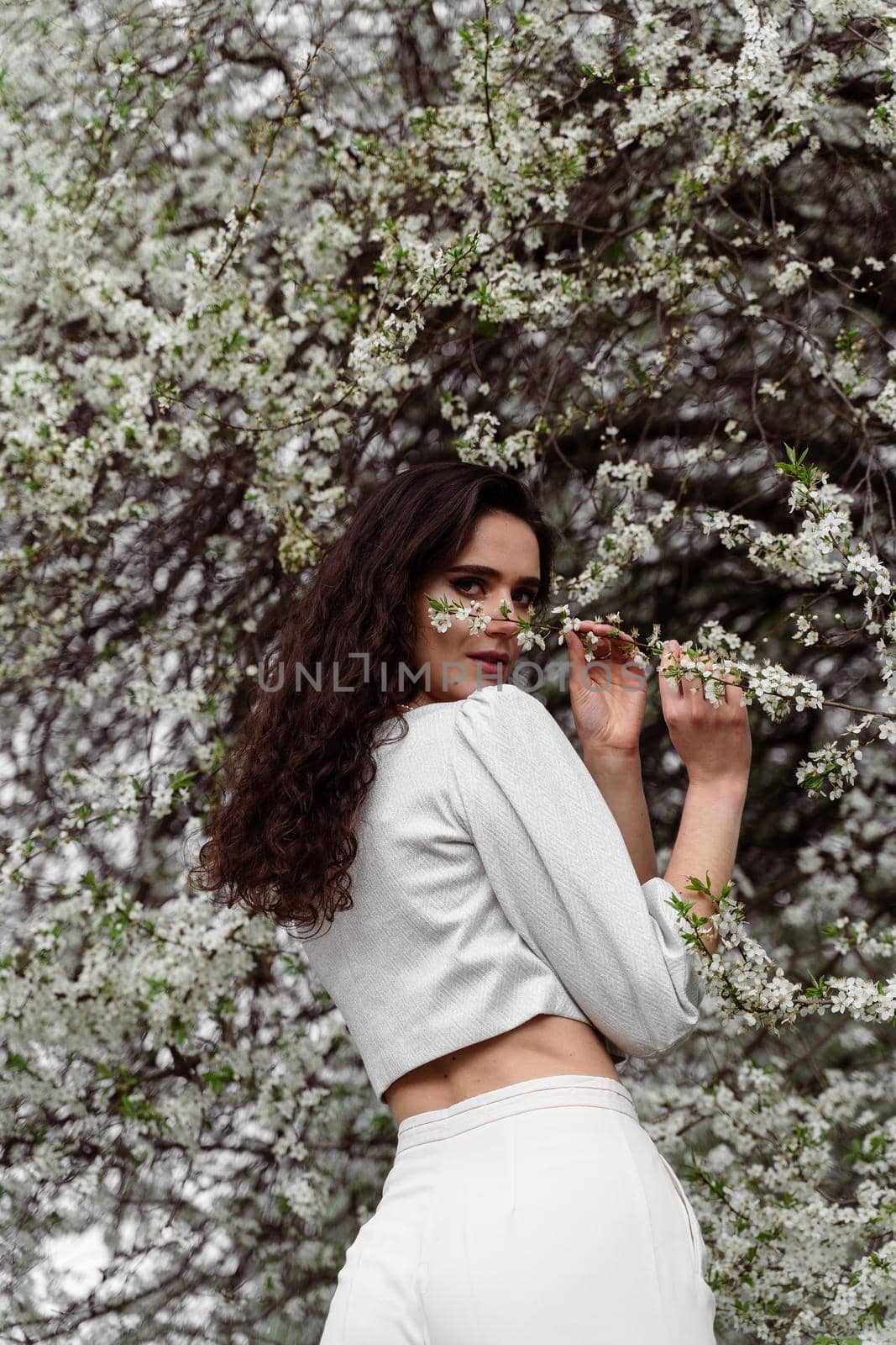 Girl touches and sniffs a branch of a white flowering tree without medical mask. Spring walking in the park