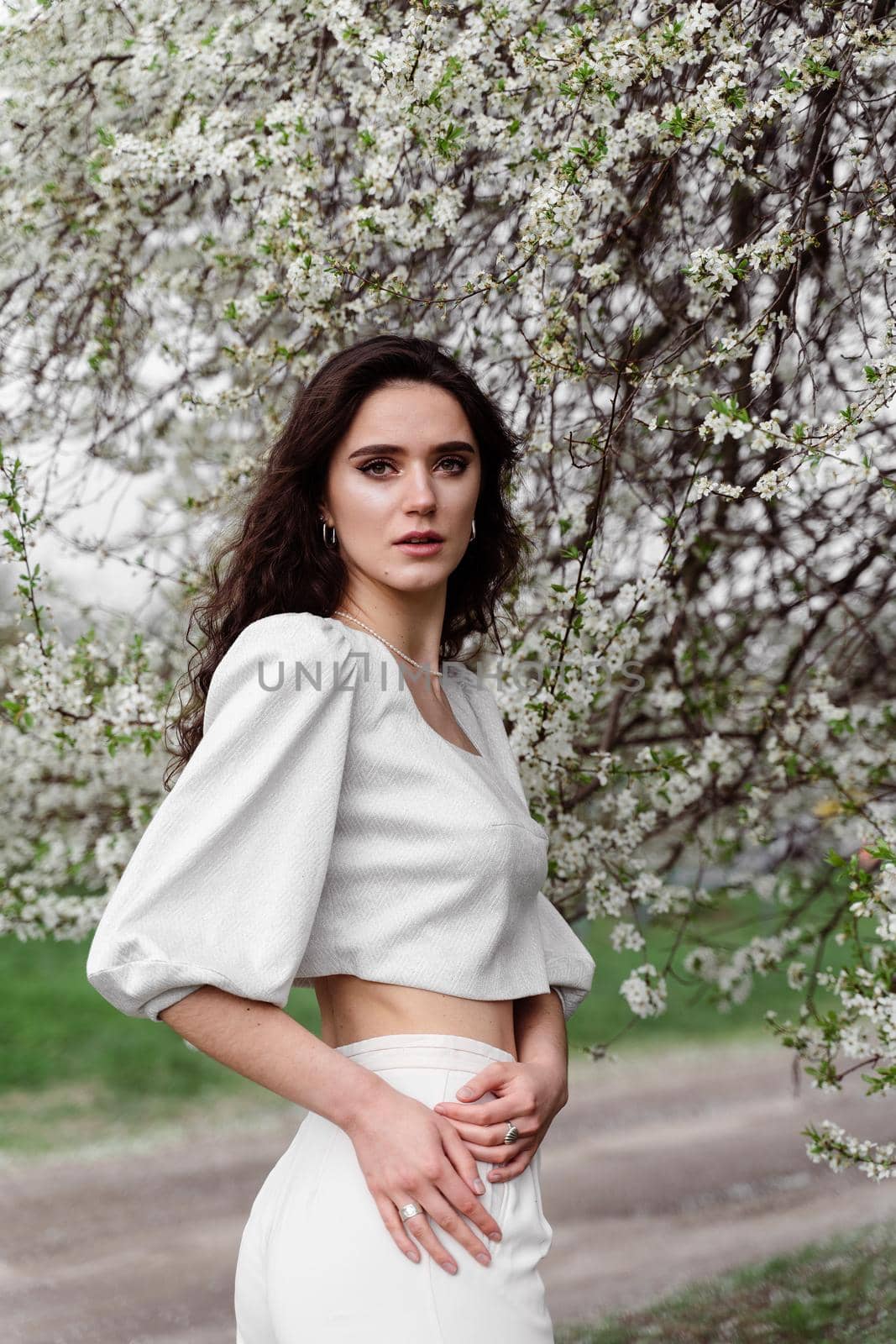 Portrait of young woman in the garden. Attractive girl weared white dress posing near blooming trees