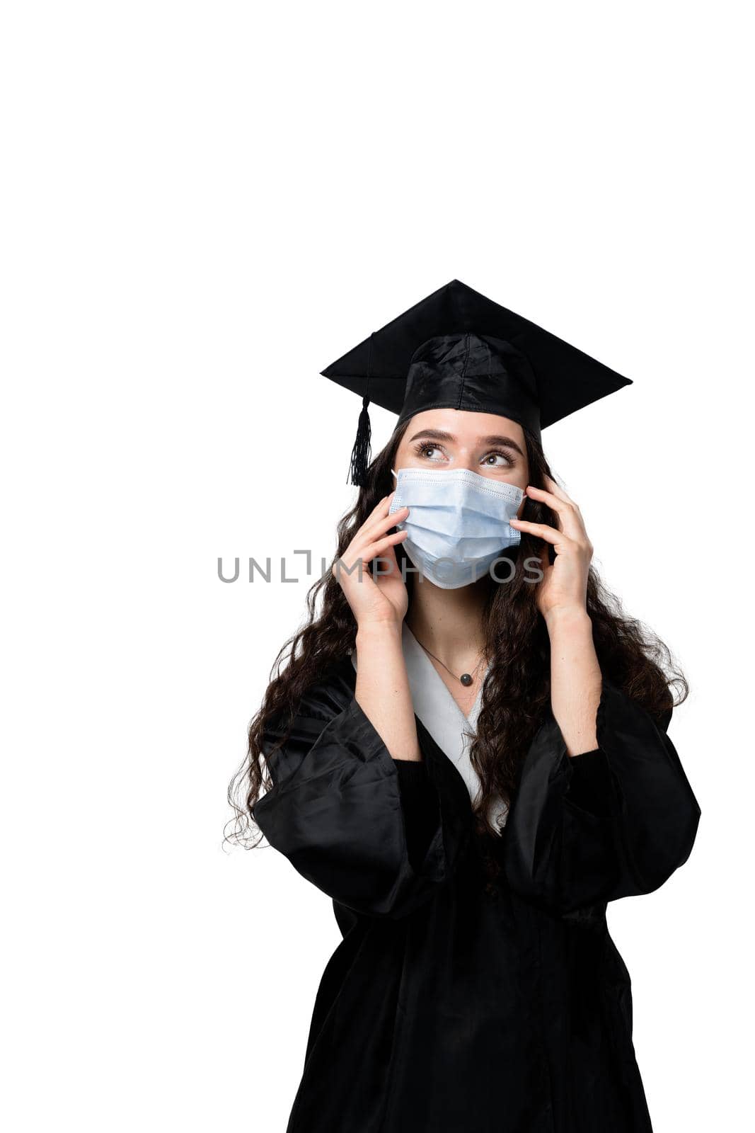 Surprised bachelor girl in medical mask at coronavirus covid-19 period. Master in graduation robe and cap on white background. Distance learning online. Study at home. Graduation from college.