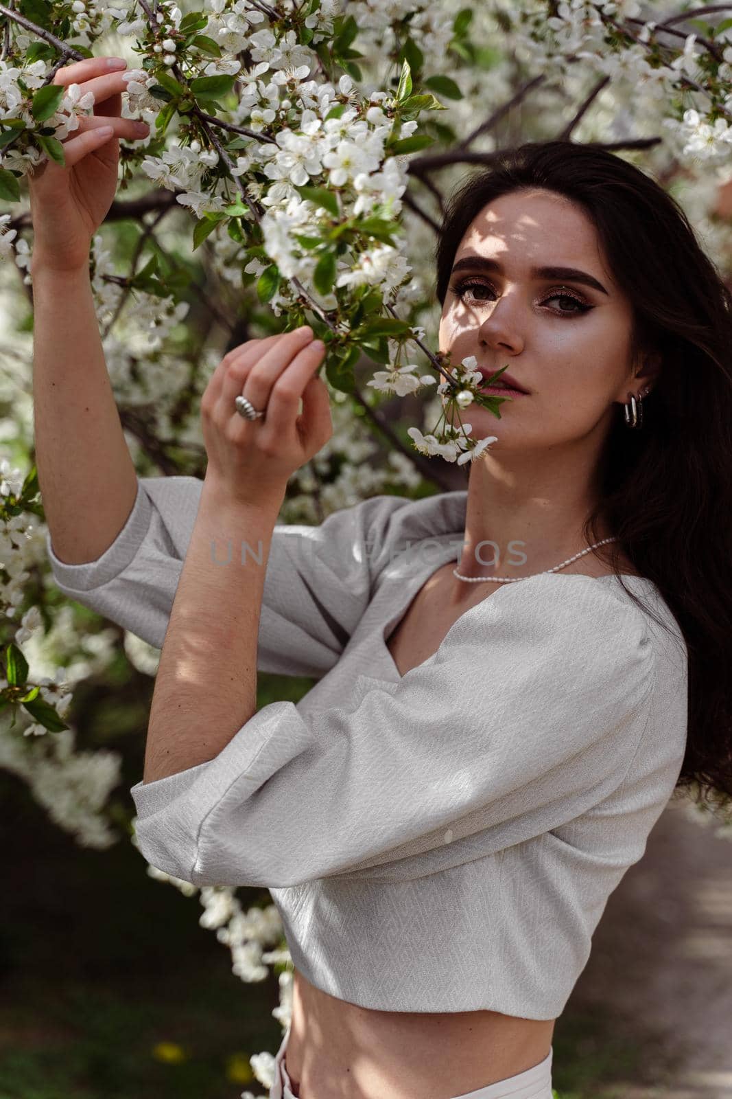 Lovely girl near blooming trees in the park. Outdoor walking in at sunny day. Lifestyle of young woman