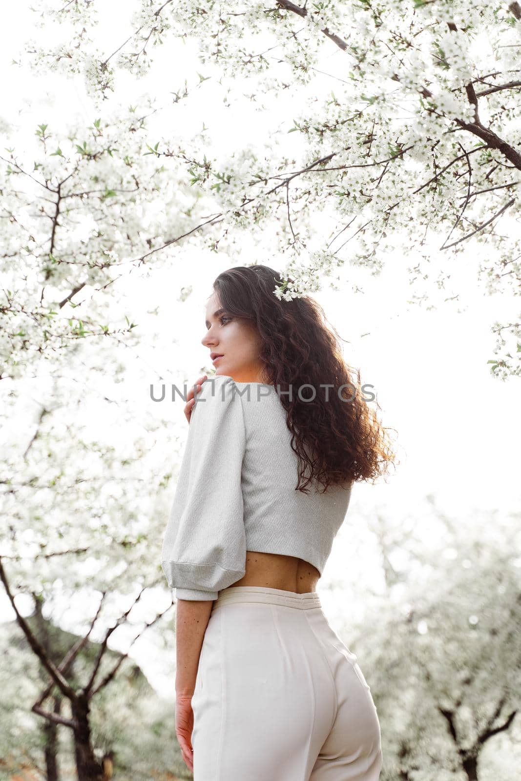 Lovely girl near blooming trees in the park. Outdoor walking in at sunny day. Lifestyle of young woman.