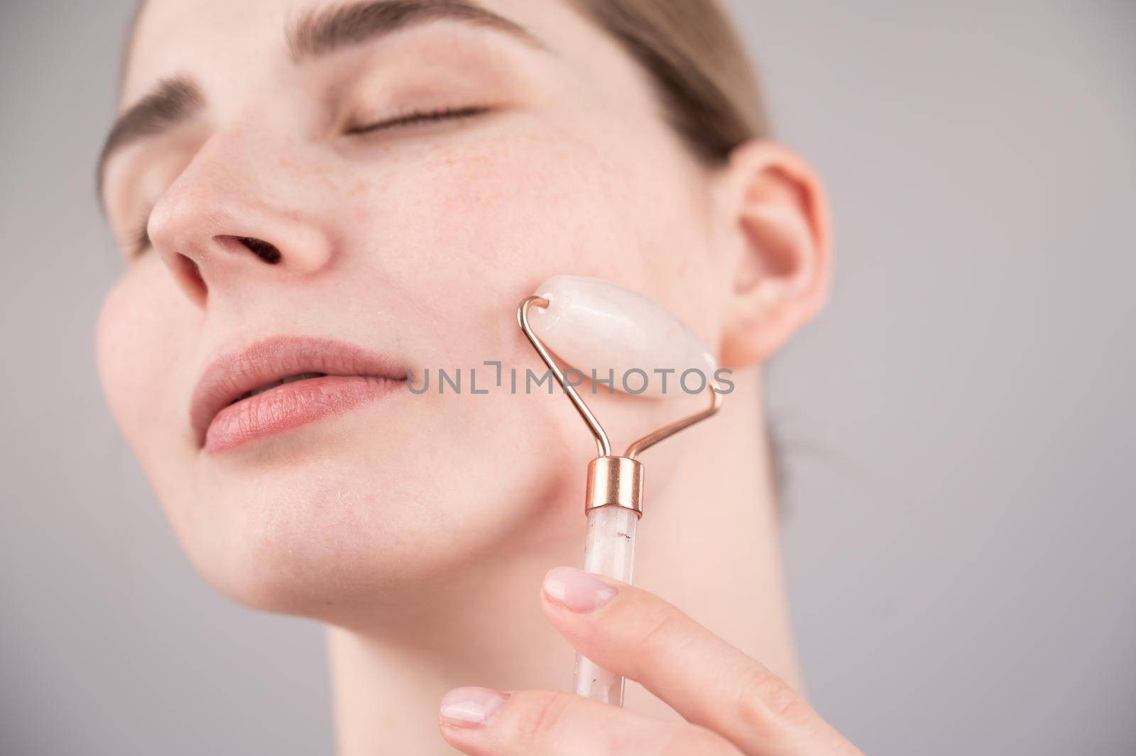 Close-up portrait of a woman using a quartz roller massager on her cheek for an alternative anti-aging