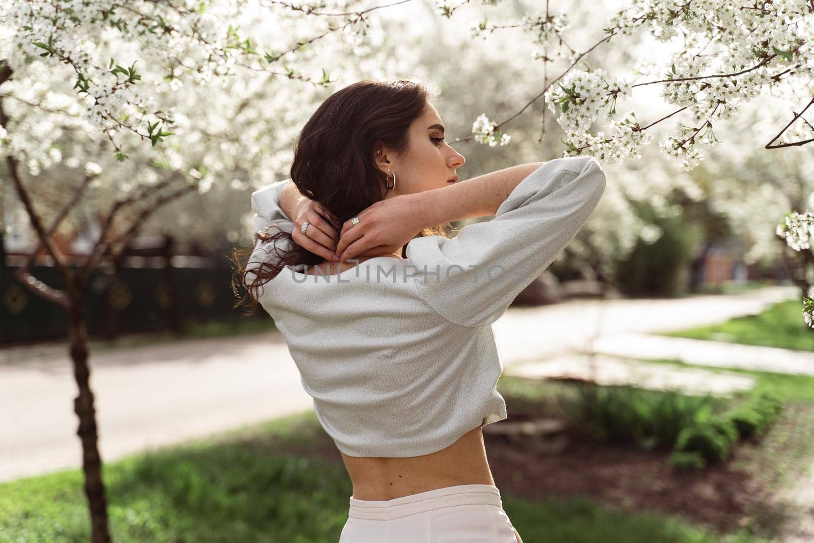 Lovely girl near blooming trees in the park. Outdoor walking in at sunny day. Lifestyle of young woman.