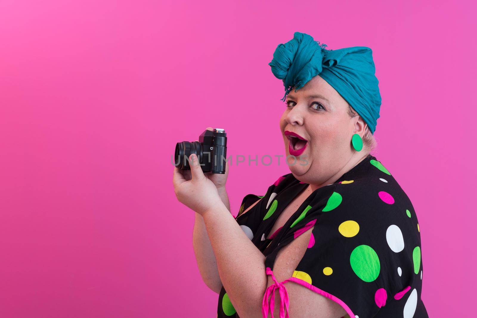 plus size smiling woman with funny emotional face expression with vintage camera in denim dress isolated on pink background, traveler on vacation, summer fashion style, excited tourist. High quality photo