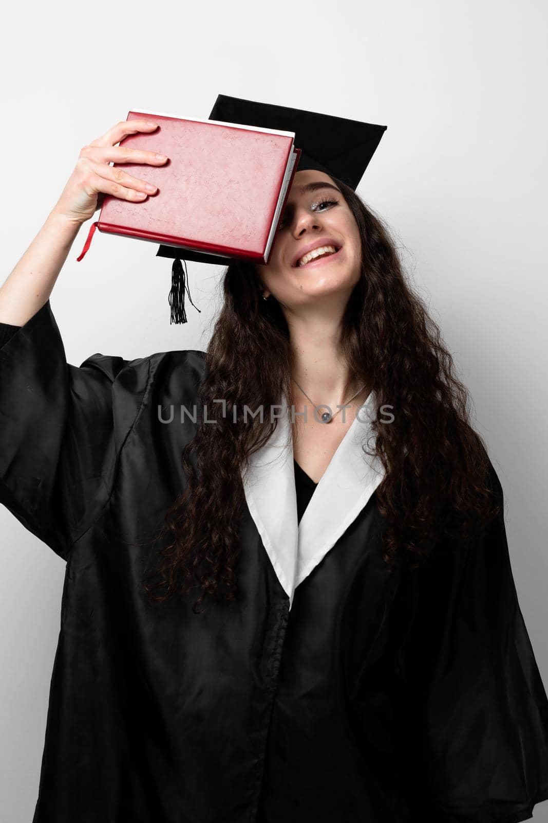 Student with book in graduation robe and cap ready to finish college. Future leader of science. Academician young woman in black gown smiling.