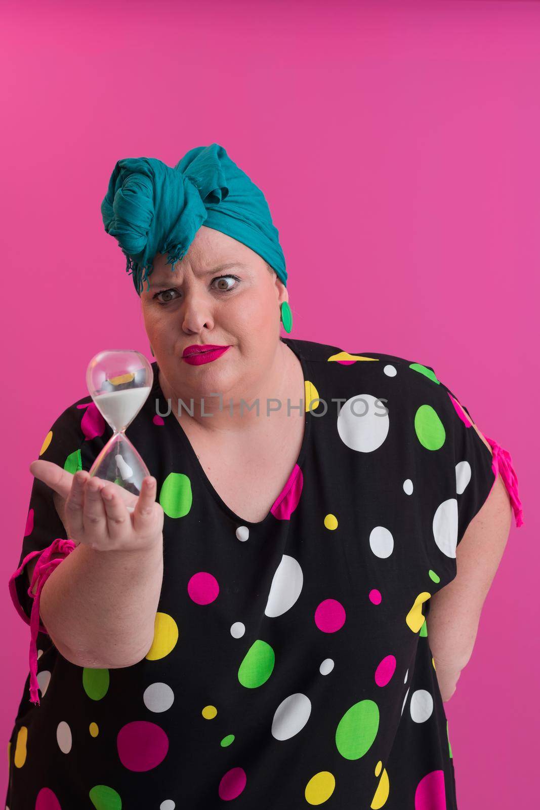 Portrait of plus size young lady smiling hands holds sand clock isolated on pink color background. High quality photo