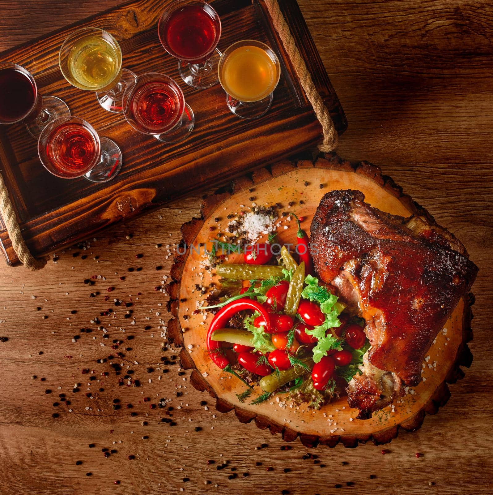 Pork knuckle with pickles, salad, vegetables, chili on a wooden board against the background of glasses with alcohol by Rabizo
