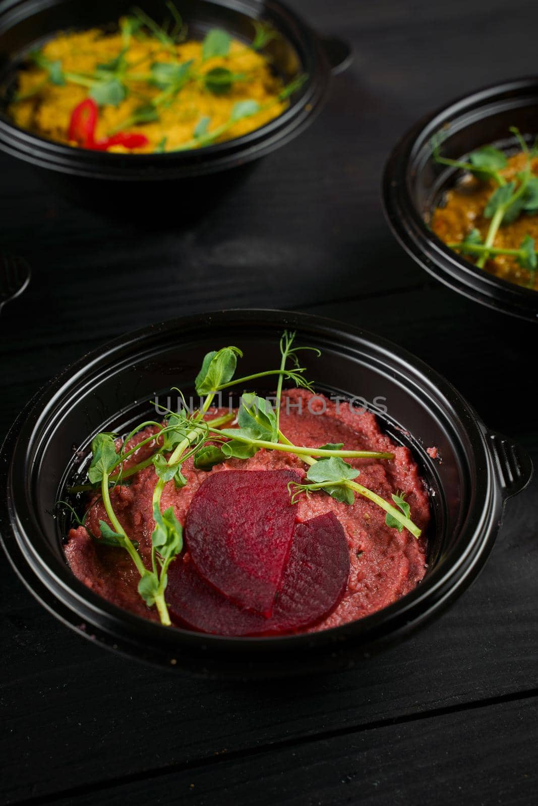 Hummus garnished peppers, chili, beet and herbs in black bowl on dark wooden table. Hummus assortment.