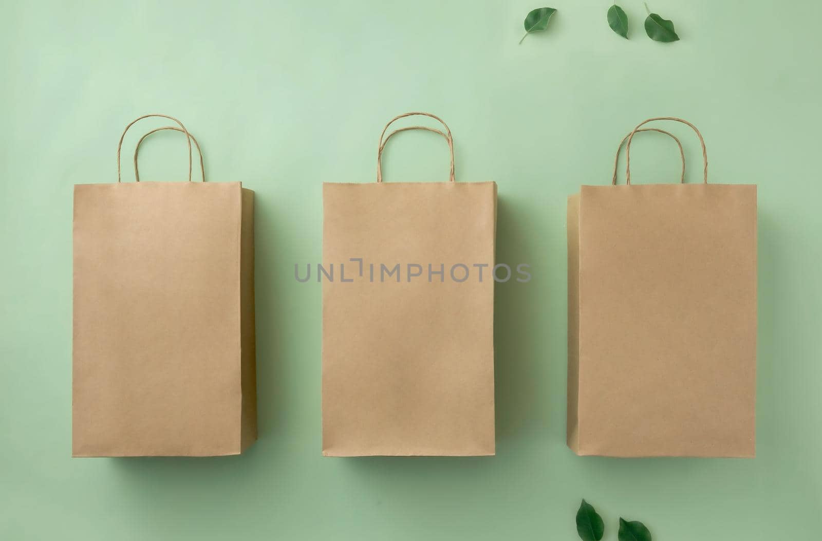 Three cardboard brown paper bags on a green eco background and green leaves. Concept of buy sell and delivery of eco product.
