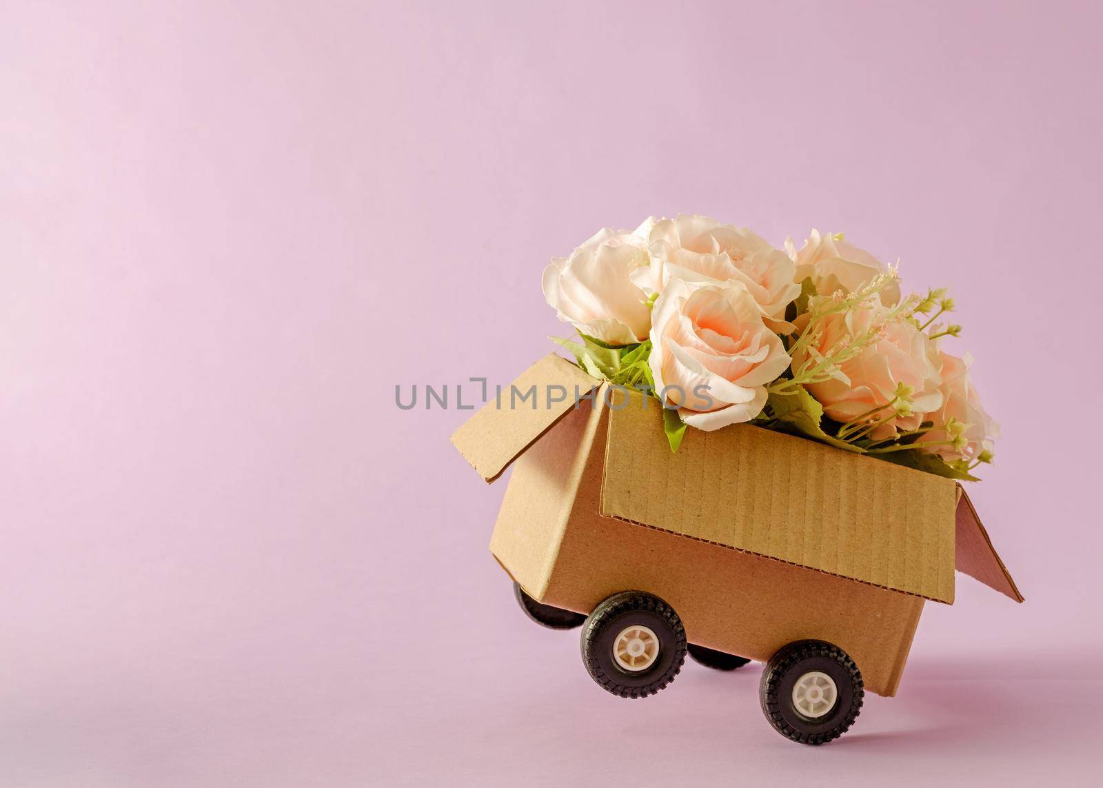 Cardboard box delivery container with truck wheels and bouquet of pink roses.  by sergii_gnatiuk