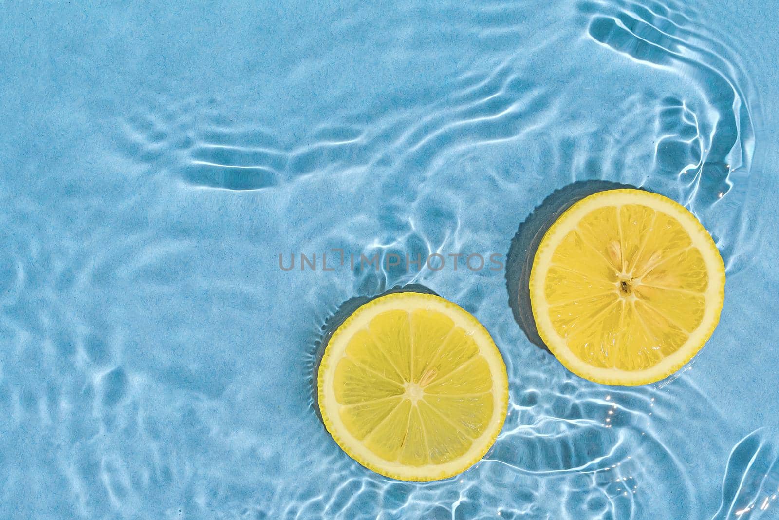 Two parts of bright yellow fresh citrus lemon fruit in blue pool with water wave motion as concept of summer vacation and healthy eating.