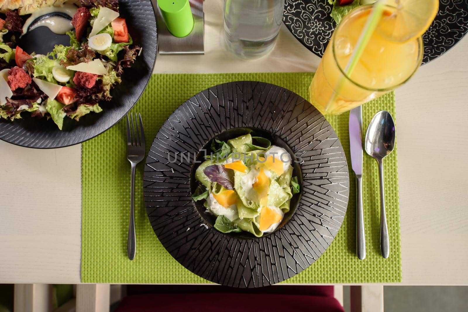 Pasta with spinach, cheese and basil on a black plate, top view. A beautiful restaurant dish. Table setting.