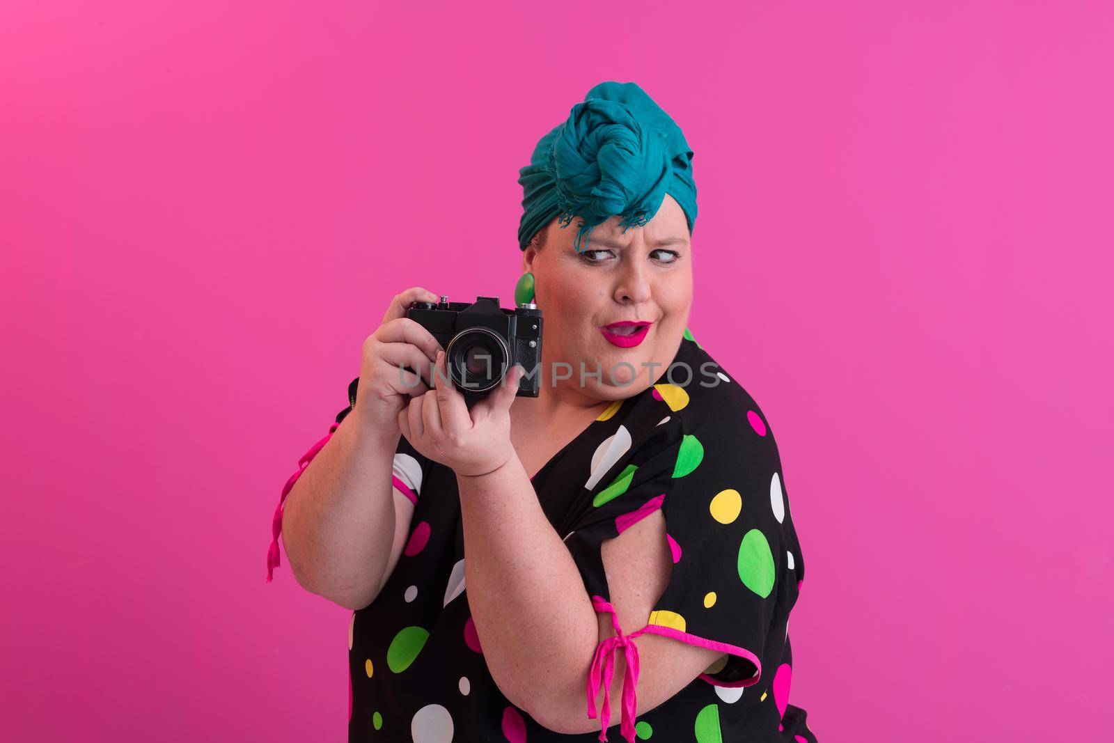 plus size smiling woman with funny emotional face expression with vintage camera in denim dress isolated on pink background, traveler on vacation, summer fashion style, excited tourist. High quality photo