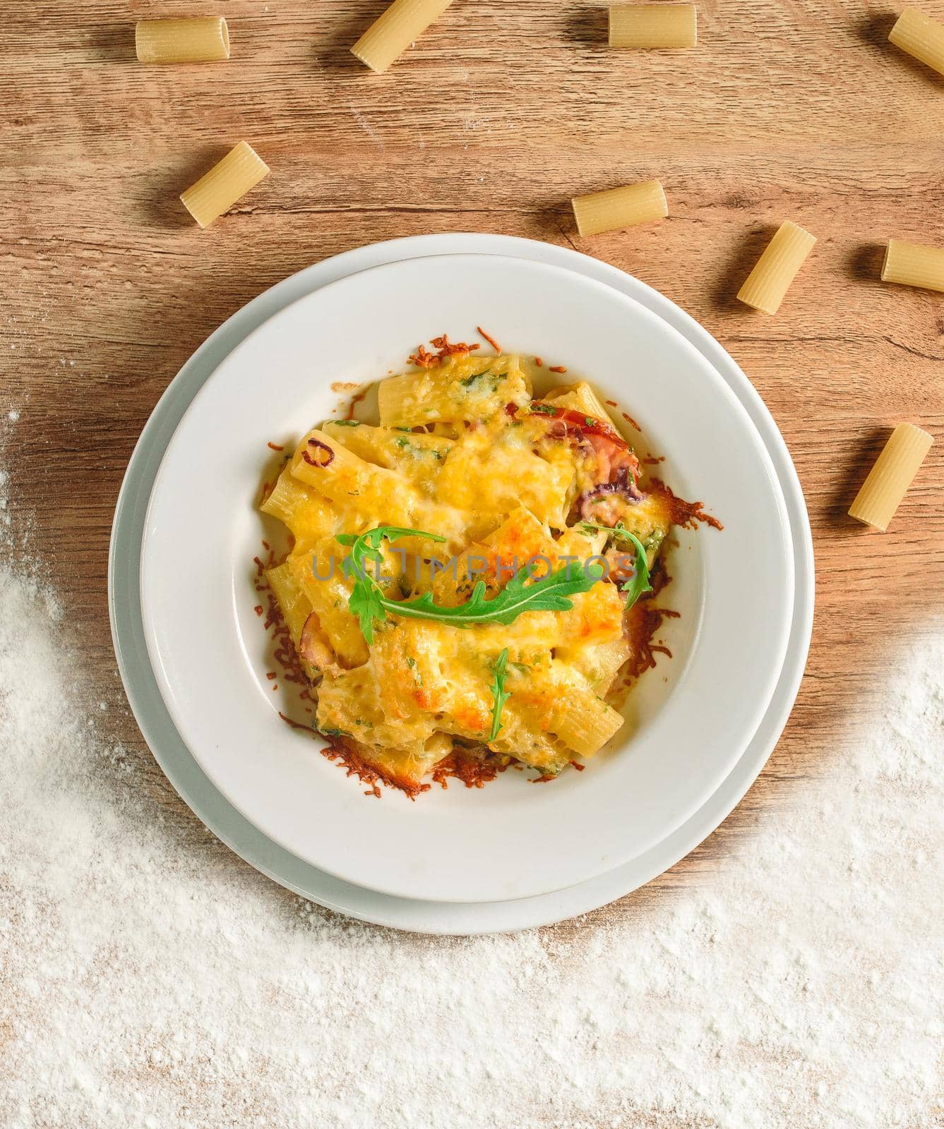 Pasta with cheese and tomato sauce on a white plate on a wooden table. Beautiful tasty restaurant food.