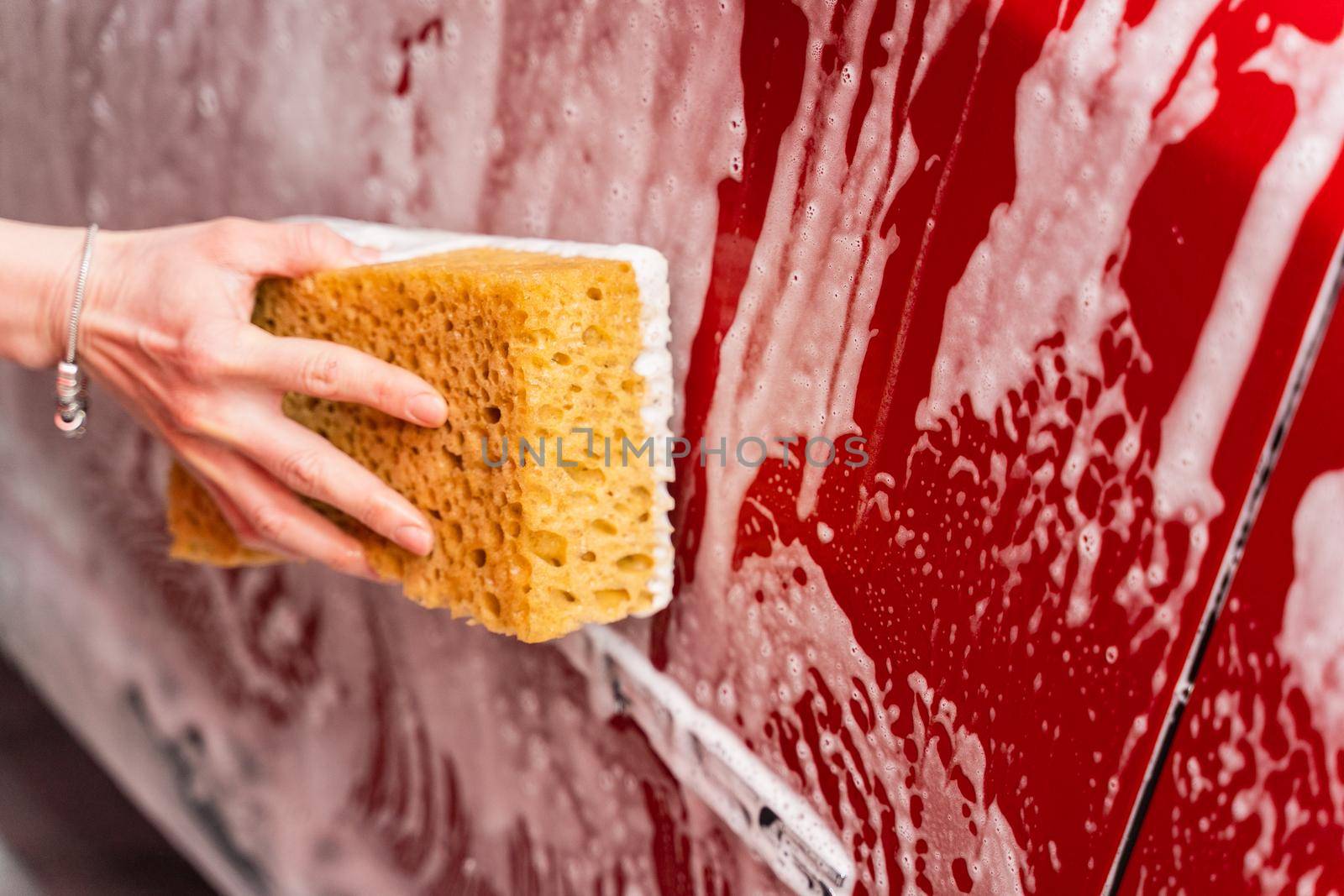 Washing a red car with a foamy yellow sponge. Woman's hand washing a car at the car wash.