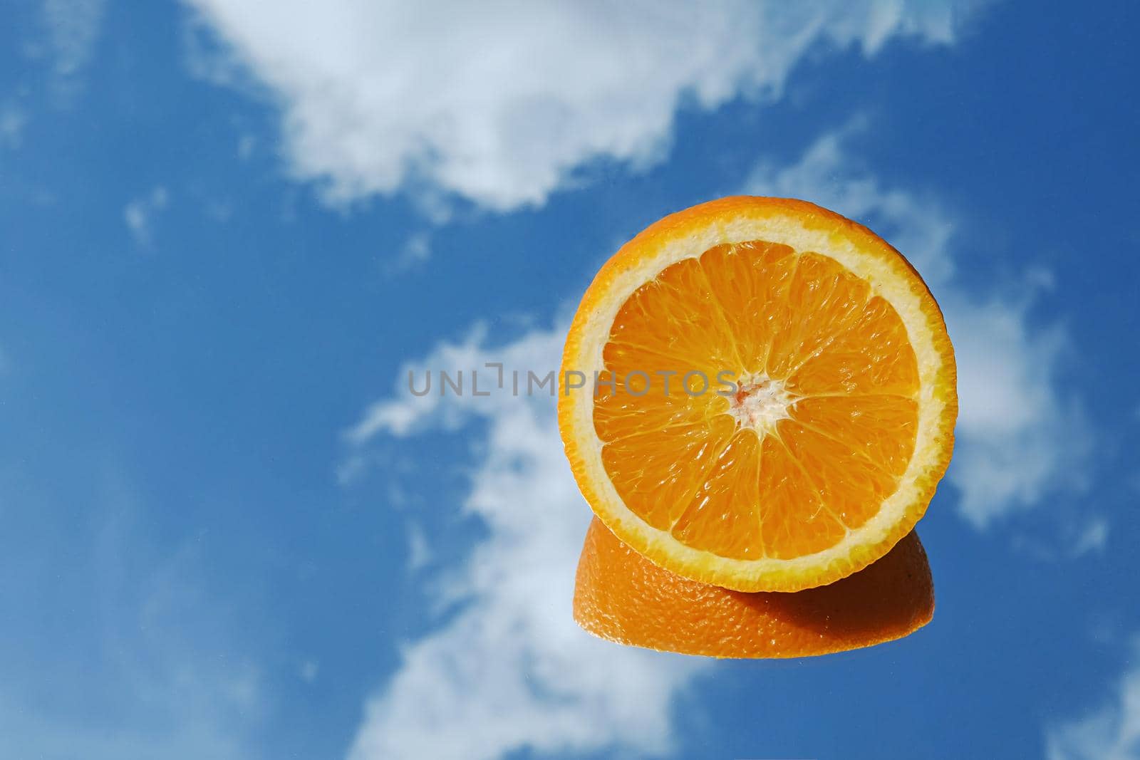 Orange citrus fruit tropical orange on blue sky and clouds background. Orange in the mirror surreal minimal concept.