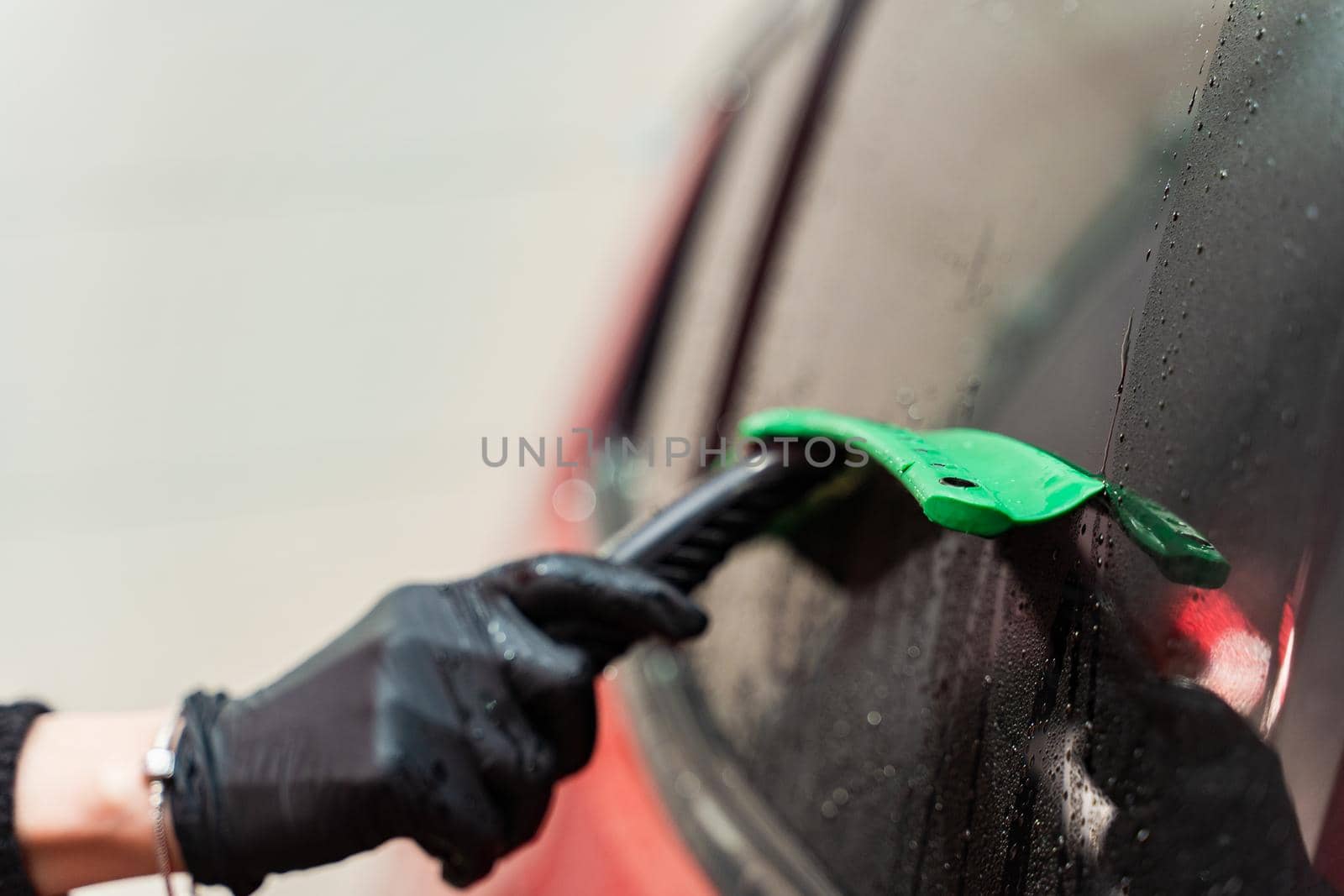 Removal of water from the glass with a rubber scraper after washing the car. Car Wash. Self-service complex. High-pressure car wash.