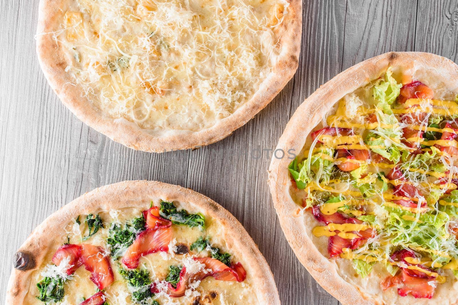 Assortment of pizza with meat, salami, prosciutto, tomatoes, dorblu cheese, mozzarella, parmesan and salad, spinach, red fish on wooden boards. Four cheese pizza, caesar, top view.