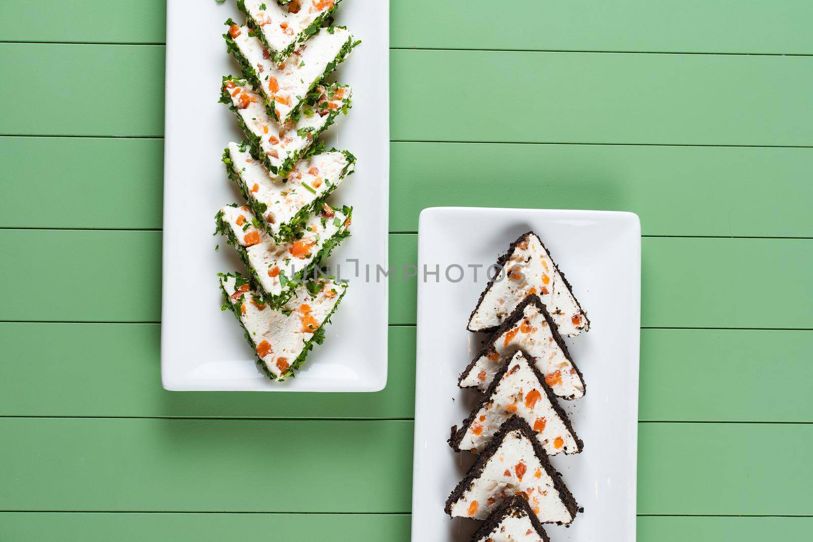 Beautiful snacks of soft cream cheese on a white plate on a green background. Cottage cheese snacks with salmon and herbs.