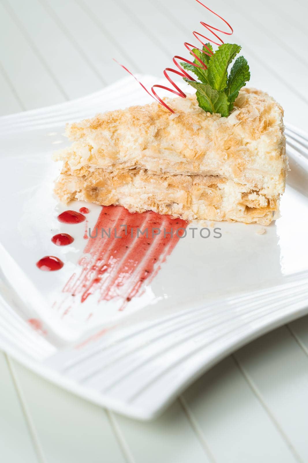 Napoleon cake decorated with a spiral of red chocolate, mint and berry jam on a white plate on a white background. Layered cake with pastry .