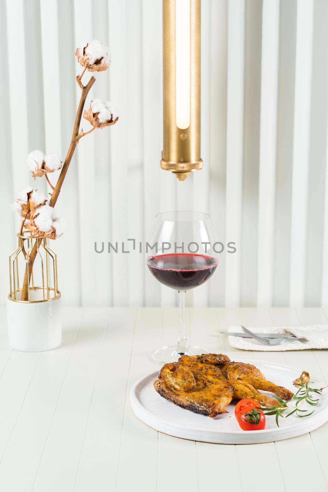 Tobacco chicken on a beautiful background with a glass of red wine, a vase with cotton twigs and a stylish lamp. by Rabizo