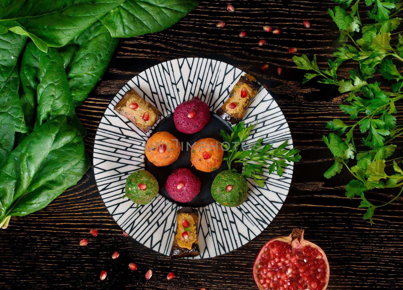 Assortment of pkhali from beets, spinach, carrots, eggplant rolls garnished with parsley and pomegranate . Georgian appetizer on a black and white plate with spinach and parsley leaves. Top view.
