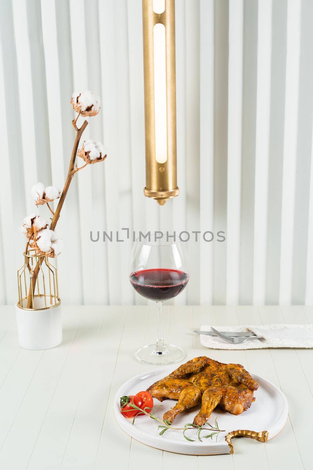 Tobacco chicken on a beautiful background with a glass of red wine, a vase with cotton twigs and a stylish lamp