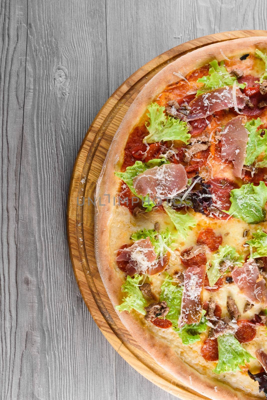 Delicious fresh italian pizza with ham, salami, tomatoes, salad and parmesan on a wooden board on a wooden table. Top view.