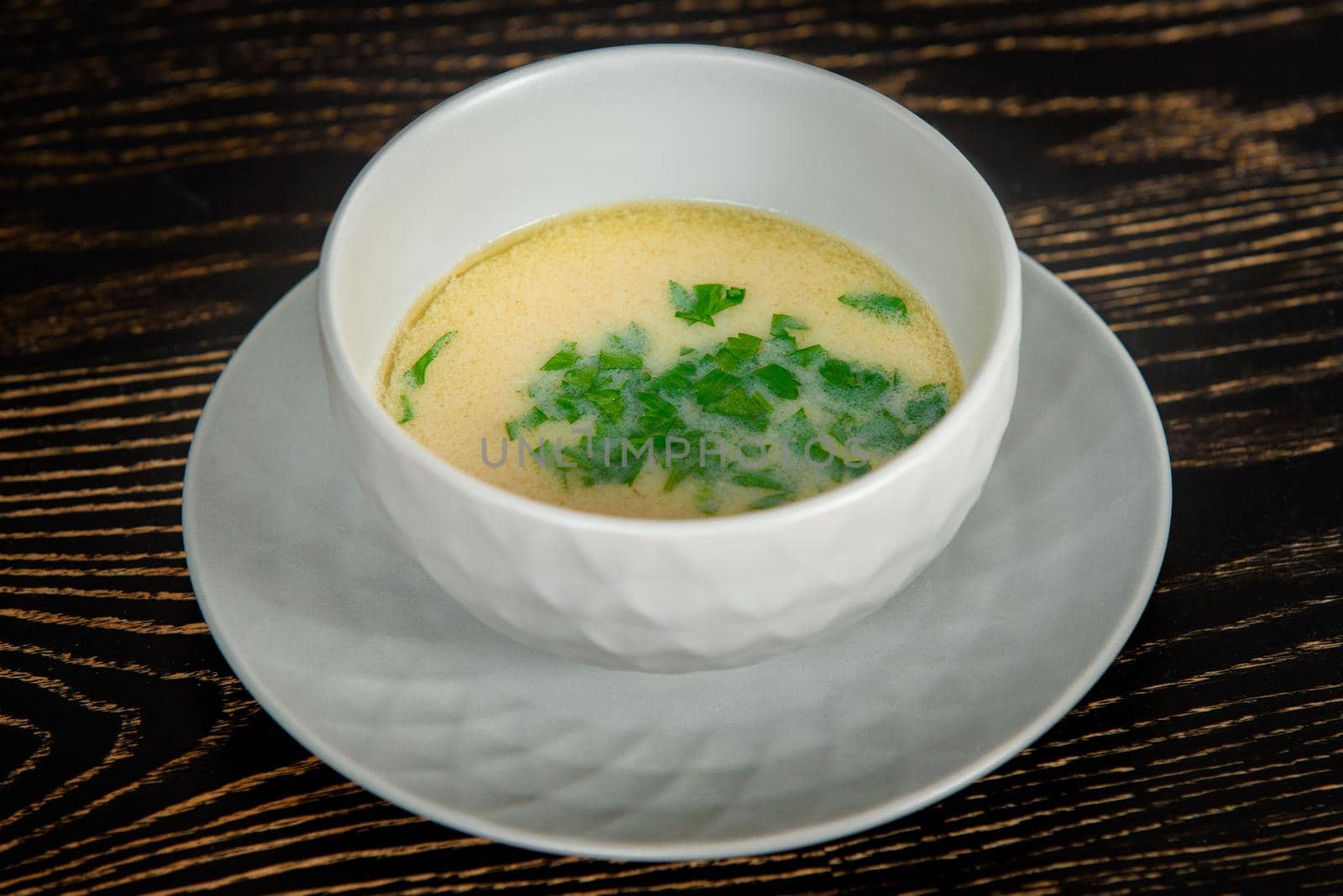 Creamy soup decorated with herbs in a gray bowl on a plate on a dark wooden table by Rabizo