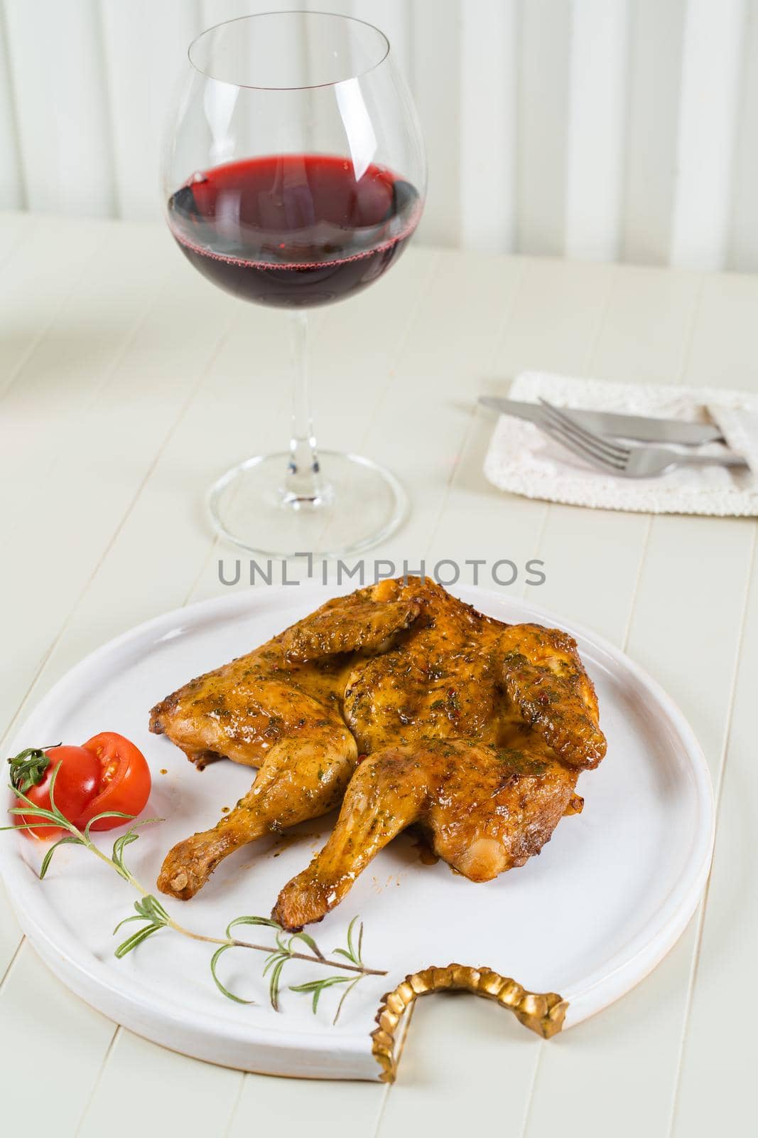 Tobacco chicken on a white plate with a glass of red wine, cutlery. Grilled chicken by Rabizo
