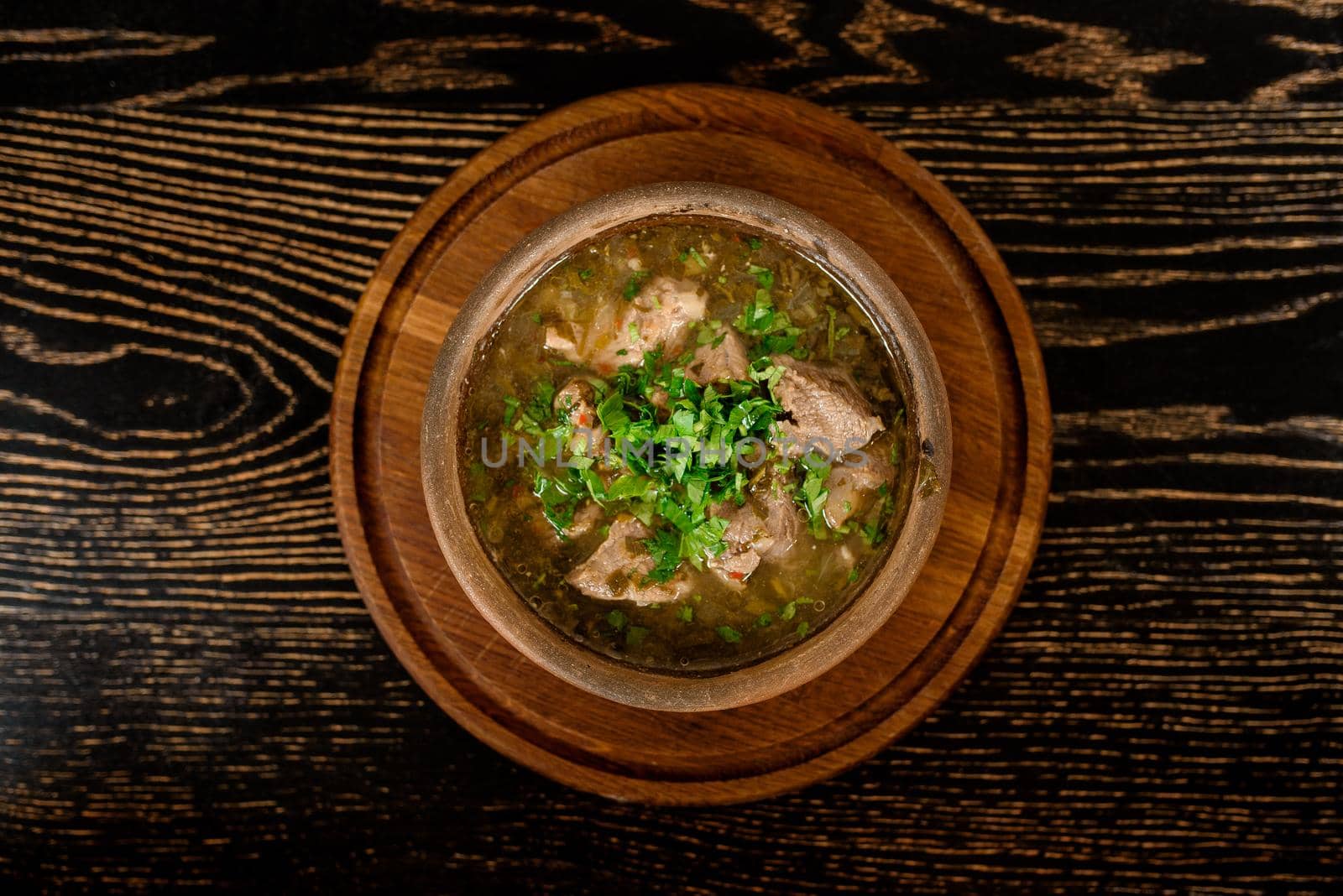 Soup with meat, sorrel and herbs on a dark wooden table. Georgian cuisine.