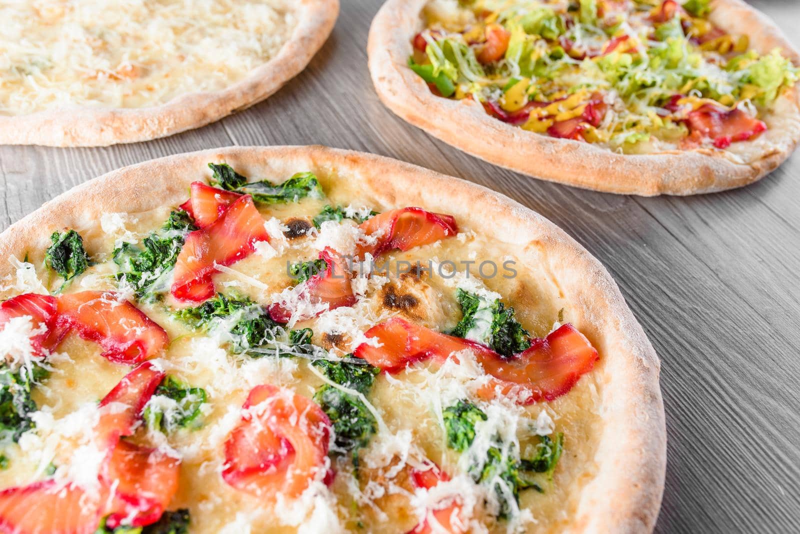 Assortment of pizza with red fish, spinach, parmesan cheese, mozzarella, lettuce, ham, four cheeses on wooden boards.